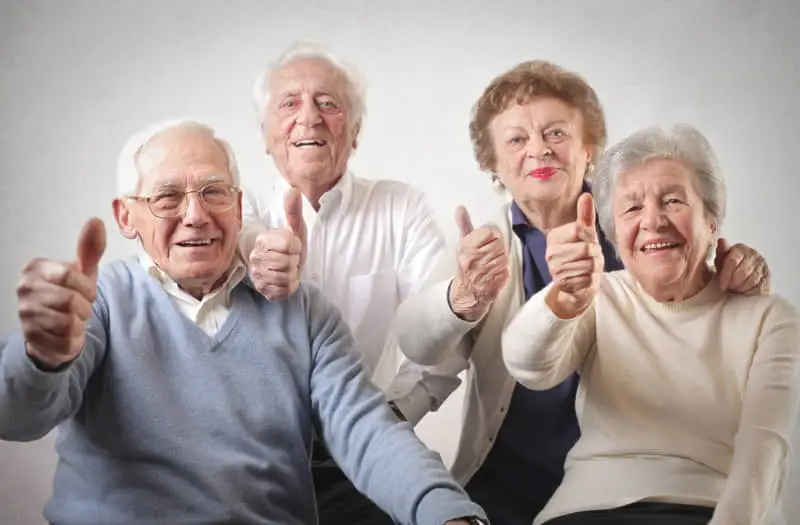 Cuatro personas mayores sonrientes mostrando pulgares arriba en señal de aprobación.